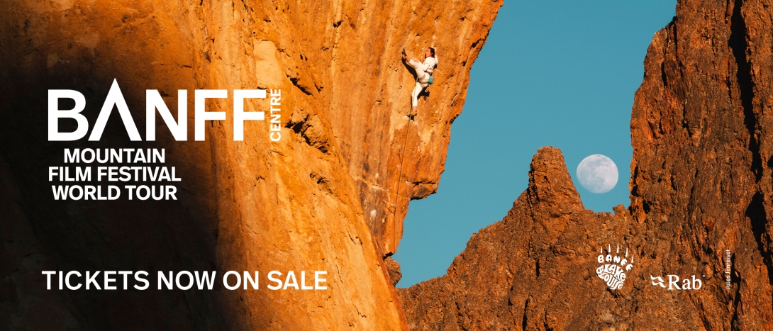 Banff Mountain Film Festival World Tour promotional banner featuring a rock climber ascending a steep orange cliff against a clear blue sky, with the Banff Mountain Film Festival World Tour logo and “Tickets Now On Sale” text.